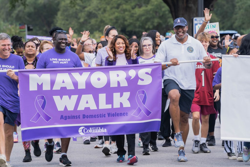 Mayor Daniel Rickenmann, Trevon Fordham, Coroner Naida Rutherford, and Solicitor Byron Gipson lead the Mayor's Walk Against Domestic Violence, holding a purple sign that reads "Mayor's Walk Against Domestic Violence."